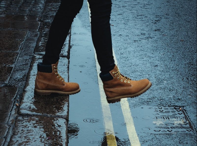 person wearing brown boots walking on a wet road